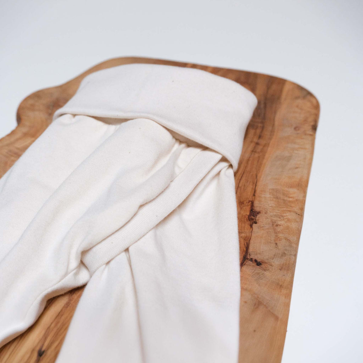 Nahaufnahme einer Abhaltehose. Detail zeigt den Schlitz und das Mitwachsbündchen am Bauch. Farbe der Hose ist natur, die Größe ist 56. Hose liegt auf Holz, das wiederum auf einem weißen Hintergrund.